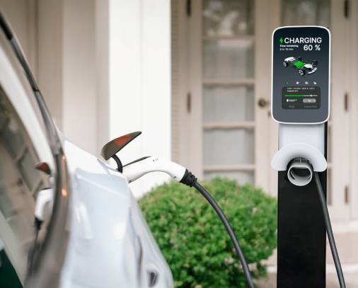 A close-up of an electric vehicle charging station displaying a 60% charge status, with a charging cable connected to a parked car.